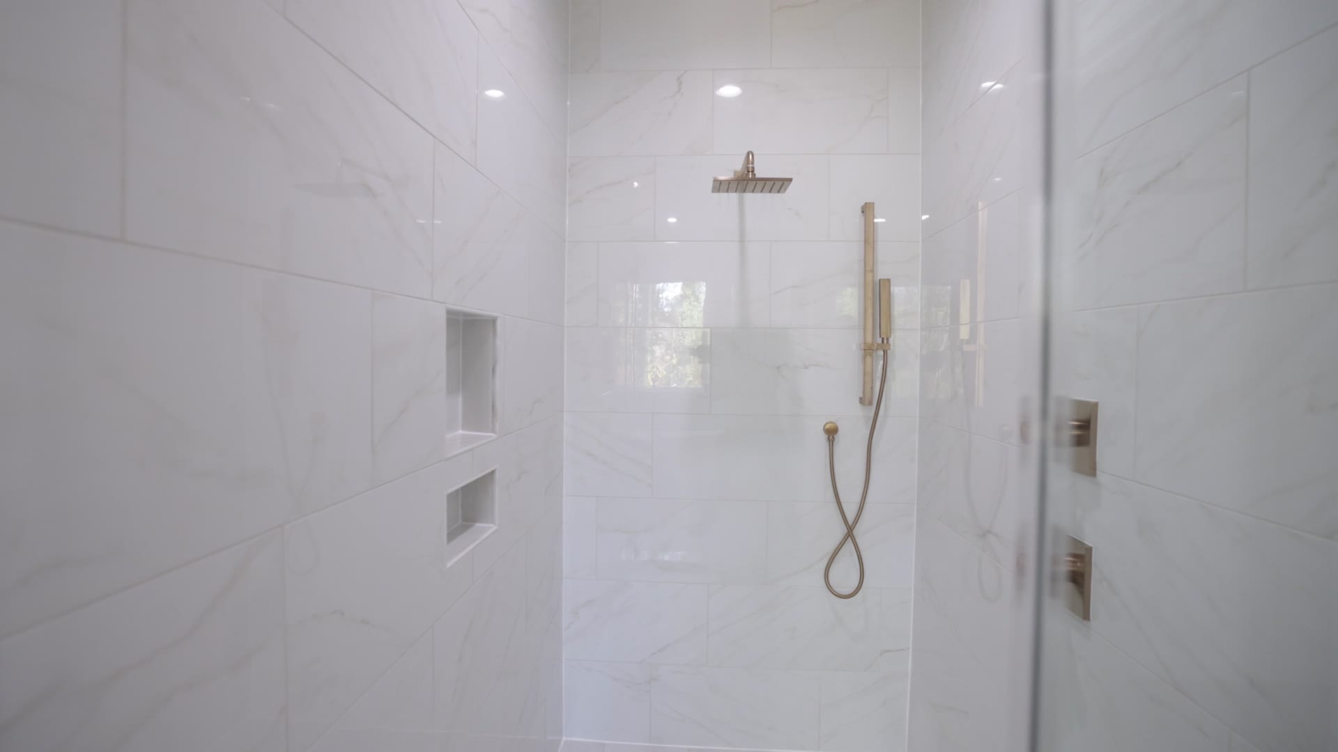 A finished marble shower: large-format porcelain, recessed niches, brushed gold rain head. Gallegos Custom Tile.