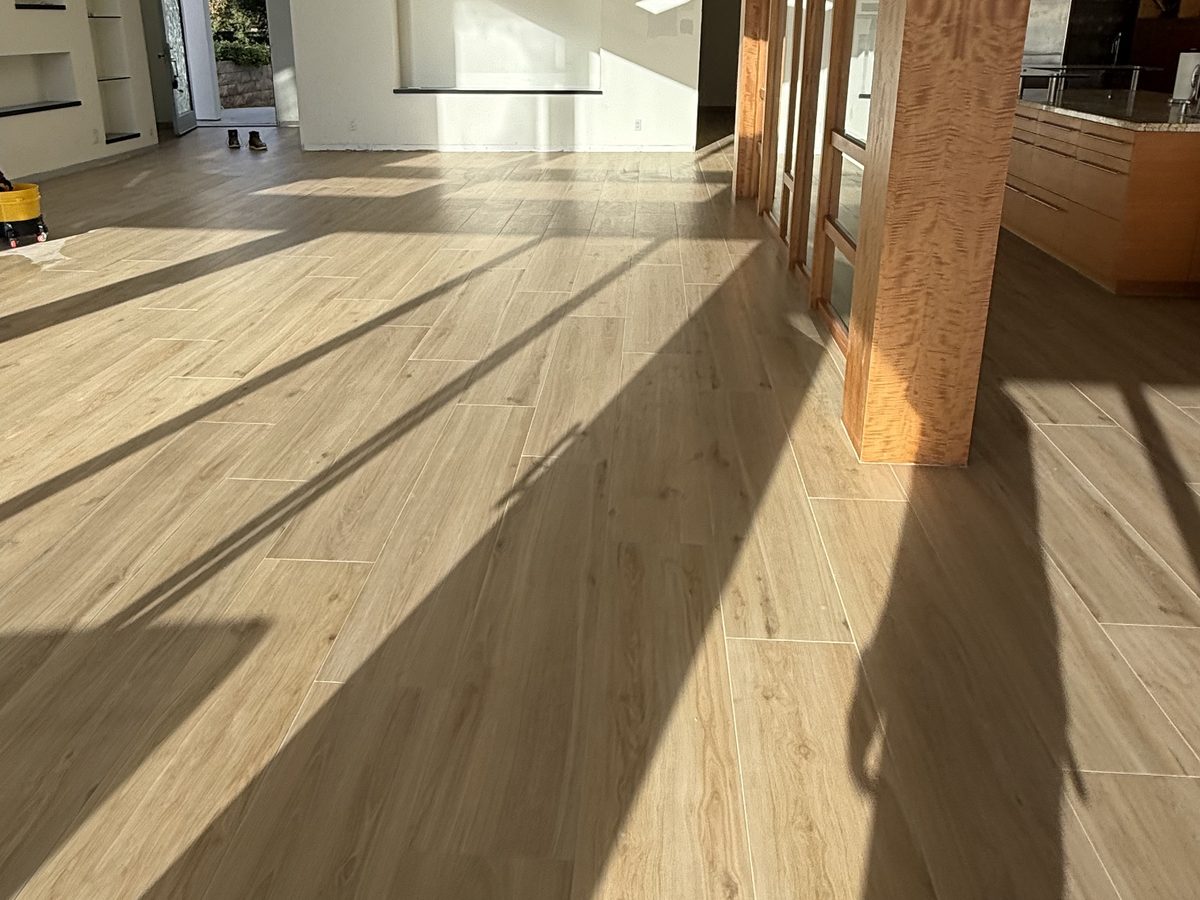 Low sun raking across wood-look porcelain plank, showing a flat surface with no lipped edges.